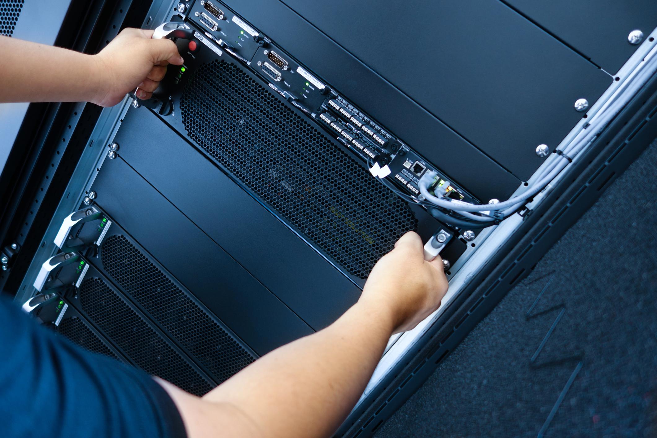 Technician installing server equipment into a rack, connecting network cables and configuring enterprise IT hardware infrastructure