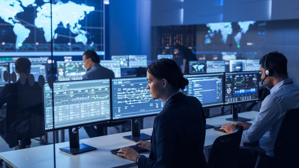 IT professionals monitoring network performance and data analytics on multiple screens in a network operations center, ensuring system security and real-time infrastructure management